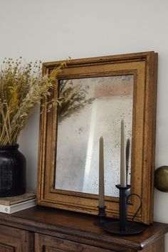 a mirror sitting on top of a wooden dresser next to a vase filled with flowers