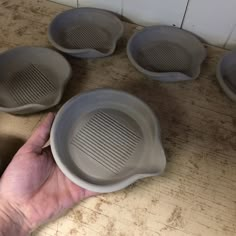 a person holding four bowls in their hand on a counter top next to other dishes