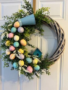 a wreath with eggs and greenery hanging on the front door, decorated with a blue birdhouse