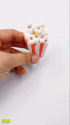 a hand holding a small cup filled with marshmallows on top of a white table