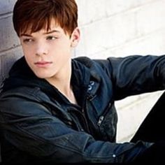 a young man leaning against a brick wall