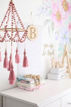 a white dresser topped with pink tassels next to a floral wallpapered wall