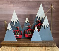 a wooden table topped with christmas trees and ski lift decorations on top of snow covered mountains