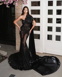 a woman standing in front of a doorway wearing a black gown with sheer detailing and an open back