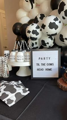 a table topped with black and white balloons, cow print napkins and a sign that says party the cows head home