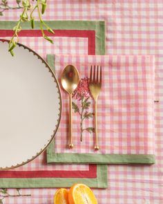 an empty plate, silverware and orange slices on a pink checkered placemat