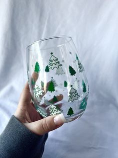 a hand holding a wine glass with christmas trees painted on it