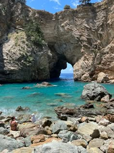 people are sitting on rocks near the water in front of an arch shaped rock formation