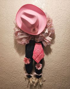 a pink hat and tie hanging on the wall next to a pair of boots with flowers