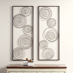 two metal art pieces hanging on the wall next to a white dresser and sideboard