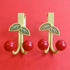 two cherries are attached to hooks on a red surface