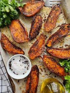 sweet potato wedges on a baking sheet with parsley and seasoning next to them