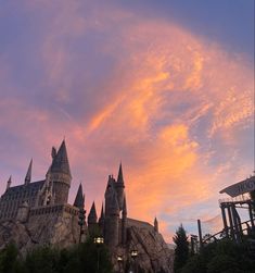 the castle is lit up at sunset with pink clouds in the sky and trees around it