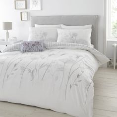 a bed with white comforters and pillows in a room next to a lamp on a table