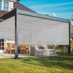 an outdoor covered patio area with furniture and table on the grass next to a house