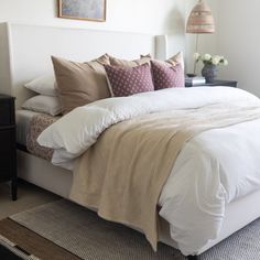 a bed with white sheets and pillows in a bedroom next to a lamp on a dresser