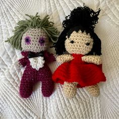 two crocheted dolls laying on top of a white bed next to each other