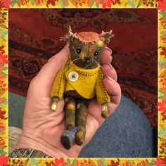 a hand holding a small stuffed animal in a yellow sweater and blue jeans with buttons on it