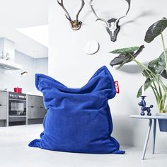 a blue bean bag sitting on top of a white floor next to a potted plant