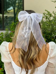 the back of a woman's head wearing a white dress with a sheer bow