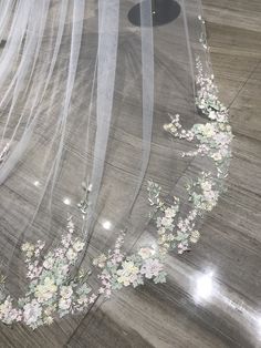 a veil with flowers on it sitting on top of a wooden floor next to a table