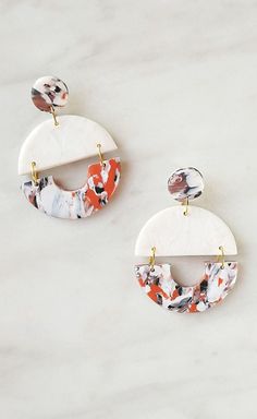 two white and orange earrings on a marble surface