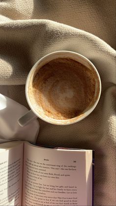 an open book with a cup of coffee next to it on top of a blanket