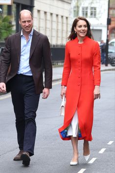 a man and woman are walking down the street in red coats, white dresses and black shoes