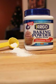 a jar of baking powder next to a spoon on a wooden table with a yellow spatula