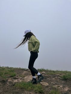 a woman standing on top of a grass covered hill next to a kite flying in the sky