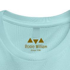 a light blue t - shirt with the rose william logo on it, in gold