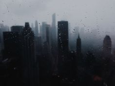 black and white photo of city skyline through raindrops on window pane with buildings in the background