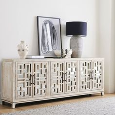 a white sideboard sitting on top of a wooden floor next to a lamp and pictures