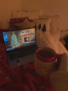 a laptop computer sitting on top of a bed next to a cup of hot chocolate