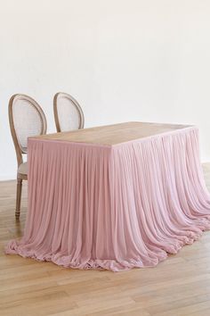 a table with two chairs and a pink cloth draped over it in front of a white wall