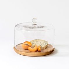 a cheese dish under a glass dome on a wooden platter with slices of fruit