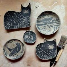 four bowls with designs on them and paintbrushes next to one that has a bird painted on it