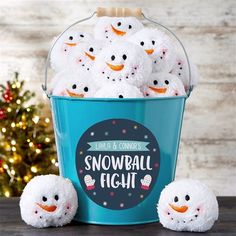 a bucket filled with snowballs sitting on top of a table next to a christmas tree