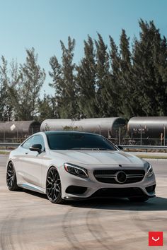 a white mercedes s - class coupe parked in front of some trees and train tracks