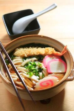 a bowl filled with noodles and vegetables next to chopsticks on a wooden table