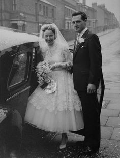 an old black and white photo of a man and woman standing next to a car