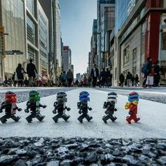 small lego figures are lined up in the middle of a street with people walking by