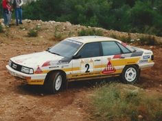 a rally car is parked on the side of a dirt road while people look on