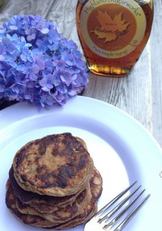 some pancakes are on a white plate next to blue flowers and a bottle of maple syrup