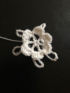 a crocheted snowflake is shown on a black surface with white thread