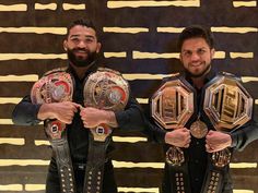 two men standing next to each other holding up their wrestling belts