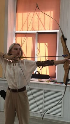 a woman is standing in front of a window with her arms outstretched holding an arrow