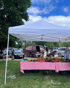 people are standing under a tent selling fruits and vegetables