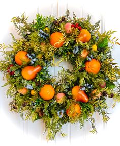 a wreath with oranges and greenery hanging on a white wooden door, surrounded by foliage