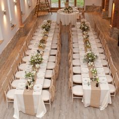 a long table set up with white linens and greenery on it for a wedding reception